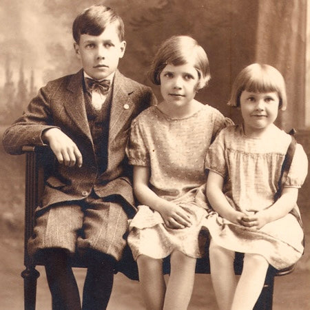 Vintage black and white photo of three children sitting on a bench.